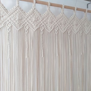 May include: A white macrame wall hanging with a geometric pattern. The hanging is made of cotton cord and is attached to a wooden dowel rod.