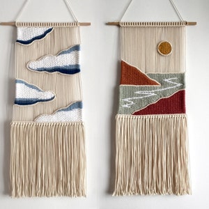 Puede incluir: Dos tapices de macramé de pared con fondo blanco y diseños coloridos. El primer tapiz de pared presenta nubes azules y el segundo presenta un paisaje rojo, naranja y verde con un sol amarillo.