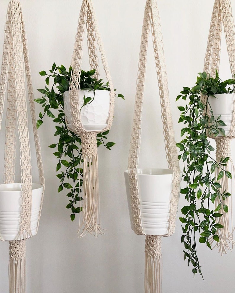 Pu&ograve; includere: Quattro portavasi in macram&egrave; con vasi in ceramica bianca e piante verdi. I portavasi sono realizzati in corda di cotone naturale e hanno un dettaglio a frangia.