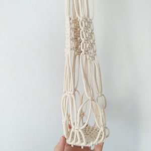 May include: A white macrame plant hanger with a round base. The hanger is made of cotton cord and has a simple, geometric design.