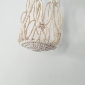 May include: A white macrame hanging planter with a circular base. The planter is made of thick cotton cord and has a woven design.