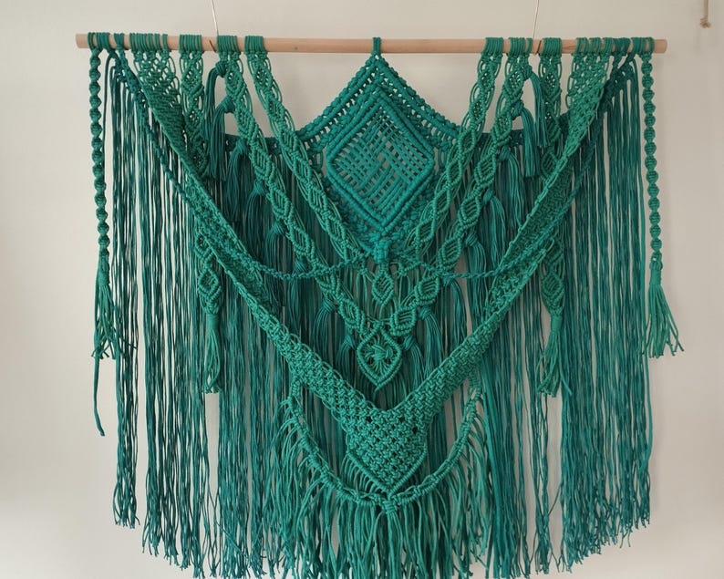 Op de afbeelding: Een tealgroene macram&eacute; wandhanger met een geometrisch ontwerp. De hanger is gemaakt van katoenen koord en heeft een franje rand.