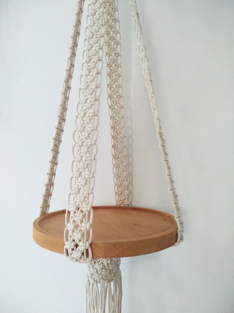 Pu&ograve; includere: Un ripiano sospeso in macram&egrave; bianco con un piano rotondo in legno. Il ripiano &egrave; sospeso al soffitto da quattro corde.