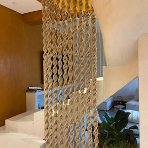 May include: A beige rope macrame wall hanging with a woven pattern. The macrame is hanging in a doorway and is partially obscured by a wooden beam.