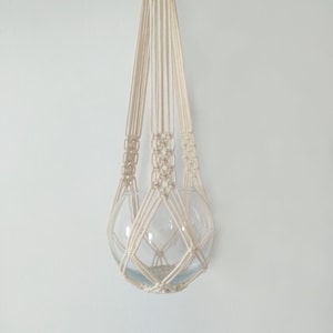 May include: A white macrame plant hanger with a glass sphere hanging from it.