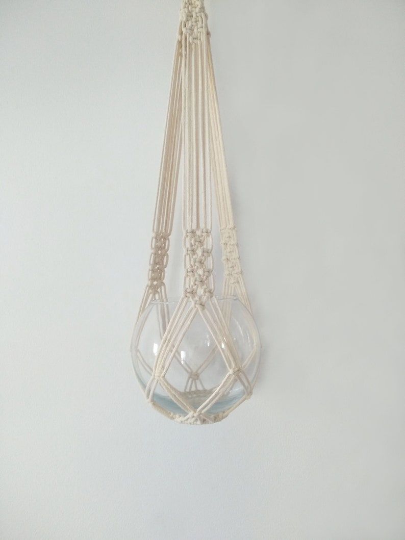 May include: A white macrame plant hanger with a glass sphere hanging from it.