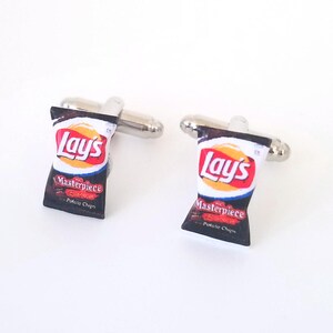 May include: A pair of silver cufflinks with a miniature Lay's potato chip bag design. The bag is black with a red and white Lay's logo and the words "Masterpiece Potato Chips".