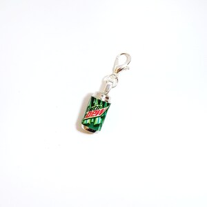 Puede incluir: Encanto de plata con forma de lata de Mountain Dew. La lata es verde con un logotipo rojo y blanco.
