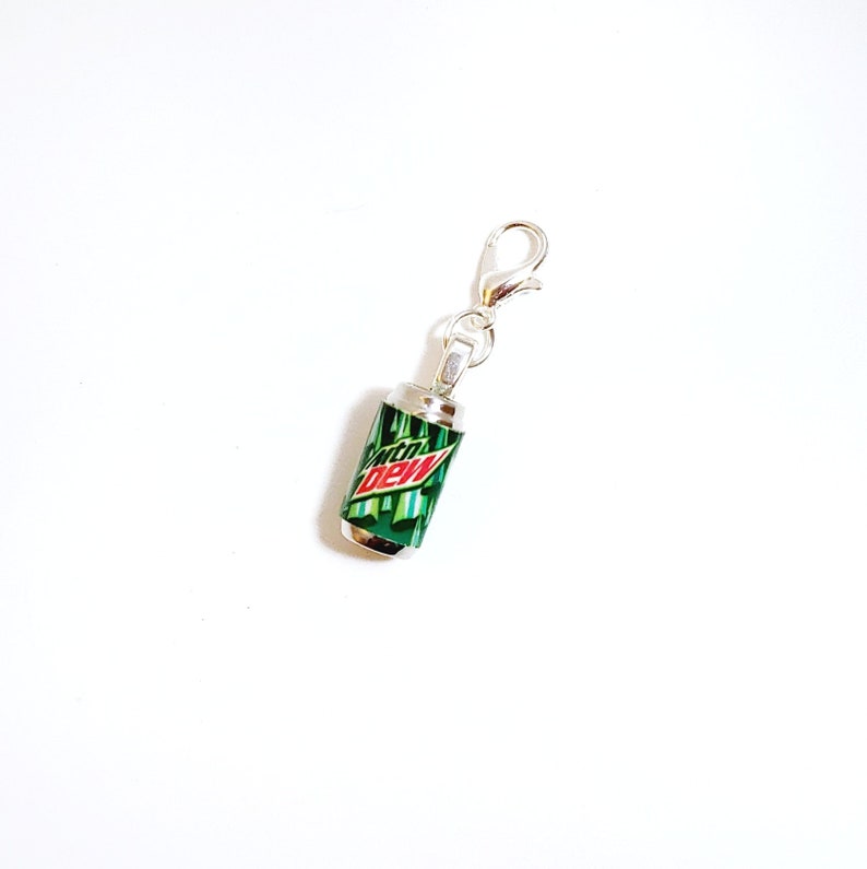 Puede incluir: Encanto de plata con forma de lata de Mountain Dew. La lata es verde con un logotipo rojo y blanco.