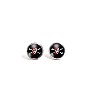 Puede incluir: Un par de pendientes de botón plateados con un diseño de calavera de pirata en blanco y negro y huesos cruzados. La calavera lleva un pañuelo rojo.
