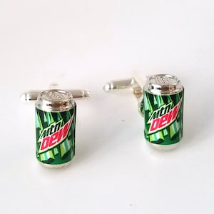 May include: A pair of silver cufflinks shaped like a Mountain Dew can. The cans are green with a white and red Mountain Dew logo.
