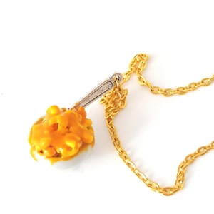 May include: A gold chain necklace with a pendant of a white bowl filled with yellow mac and cheese and a silver spoon.