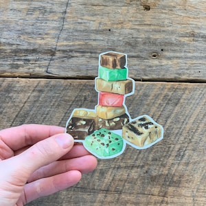 May include: A stack of colorful fudge squares with different flavors, including chocolate, mint, and caramel. The fudge is arranged in a pyramid shape and is ready to be enjoyed.