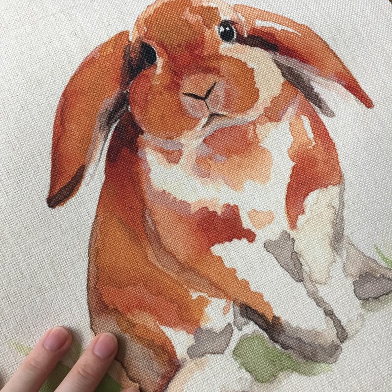 Puede incluir: Pintura acuarela de un conejo marr&oacute;n y blanco con orejas ca&iacute;das. El conejo est&aacute; sentado sobre un fondo verde.
