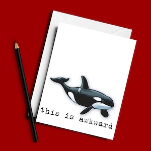 May include: A white card with a black and white illustration of an orca whale swimming. The text "this is awkward" is printed in black typewriter font.