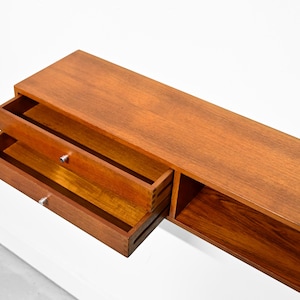 May include: A long, rectangular wooden shelf with two drawers and a lower open shelf. The drawers are open, revealing the interior. The wood has a warm, reddish-brown tone, and the hardware is silver. The shelf is set against a white background.