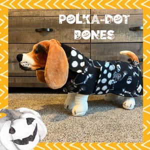 May include: A black and white dog costume with a polka dot pattern and skeleton design. The text "POLKA-DOT BONES" is written above the dog.