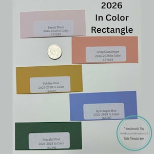 May include: A collection of color swatches in various shades, including pink, peach, gold, blue, and green, with labels indicating color names and codes. The text "2026 In Color Rectangle" is displayed at the top. A quarter coin is included for size reference.