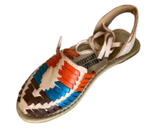 May include: A pair of woven leather sandals with a brown, blue and orange pattern. The sandals have a lace-up closure and a beige leather strap around the ankle.
