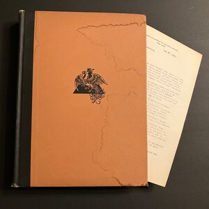 May include: A brown book with a black spine and a black and white illustration of a bird on the front cover. The book is titled "The American Museum of Natural History, New York, May 27, 1921."