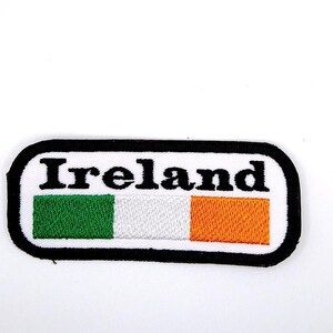 May include: A black and white rectangular patch with the word "Ireland" in black text and an embroidered Irish flag in green, white, and orange.