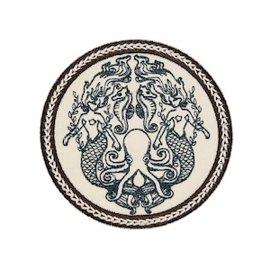 May include: A round, brown embroidered patch with a white background. The patch features a design of two mermaids flanking an octopus, all in a dark blue colour.
