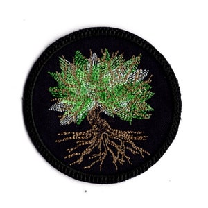 Könnte beinhalten: Ein runder schwarzer Patch mit einem gestickten Baum in Grün und Braun. Der Baum ist stilisiert und hat eine kreisförmige Form.
