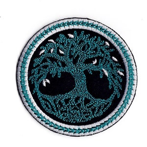 May include: A round, embroidered patch featuring a teal tree of life design on a black background. The tree is encircled by a white and teal stitched border.