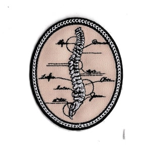 Könnte beinhalten: Ein beigefarbener gestickter Aufnäher mit schwarzem Rand. Der Aufnäher zeigt eine detaillierte Illustration einer menschlichen Wirbelsäule mit beschrifteten Wirbeln.