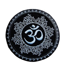 Peut inclure: Un patch brodé noir avec un symbole Om blanc entouré d'un motif floral décoratif.