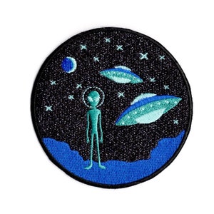 May include: Round embroidered patch featuring an alien figure with a halo, standing before two UFOs. The background is a starry night sky with a blue planet and a blue and black border. The patch is suitable for jackets, bags, or other fabric items.