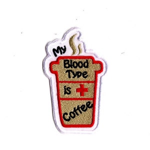 May include: Embroidered iron-on patch with a coffee cup design. The cup is brown and white with red trim. The text on the patch reads "My Blood Type is Coffee".