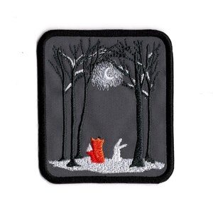 Op de afbeelding: Gestikt patch met een vos en een konijn die in een bos onder een halve maan staan. Het patch is grijs met zwarte stiksels en de dieren zijn rood en wit.