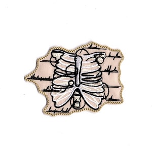 May include: A beige fabric patch with a black and white embroidered image of a rib cage.