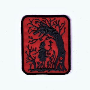 May include: A red embroidered patch featuring a black silhouette of a girl holding a basket of flowers standing in front of a tree with a wolf's head. The tree is on a red background.