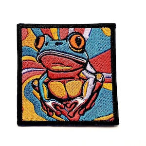May include: Embroidered patch featuring a colorful frog with large orange eyes. The frog is set against a vibrant background of swirling red, yellow, and blue patterns, all framed by a black border. This patch is ideal for adding a unique touch to clothing or accessories.