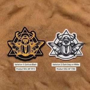 May include: Two embroidered patches featuring a stylized scarab beetle design. One is gold on black, the other dark gray on white. Each patch has a geometric border and the text "Variation 1: Gold-on-Black" and "Variation 2: Dark Gray on White".