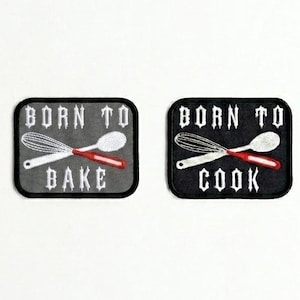 May include: Two embroidered patches with the text "BORN TO BAKE" and "BORN TO COOK". Each patch features a whisk and spoon with red accents. The patches are square with rounded corners and a black border.