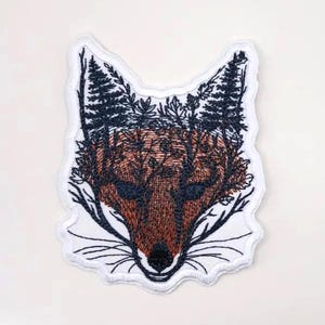 May include: Embroidered patch of a fox's face with a forest scene inside the outline of the fox. The fox is brown and the forest is black.