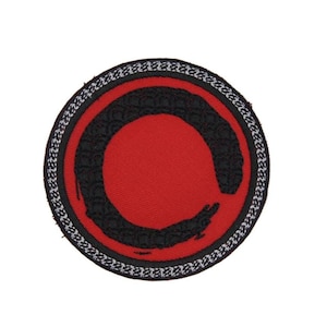 May include: A red and black embroidered patch with a circle design. The circle is outlined in black and has a white border.