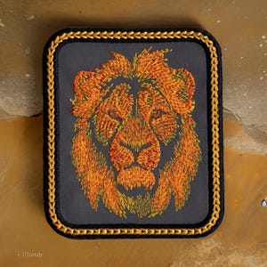 May include: A black embroidered patch with a gold border featuring a lion's head with orange and yellow fur.