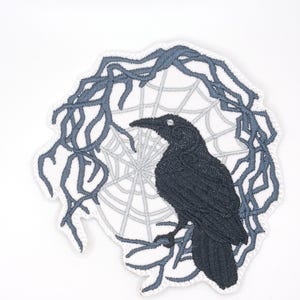 May include: Embroidered patch featuring a black crow perched on a branch within a spiderweb design. The crow is detailed with textured stitching, set against a white background. The web and branch are in shades of gray and blue.