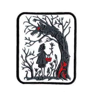 Peut inclure: Un écusson brodé rectangulaire à fond blanc et bordure noire. Le motif représente la silhouette gris foncé d'un personnage en cape à capuche tenant un panier rouge, debout sous un grand arbre torsadé avec une créature ressemblant à un loup.