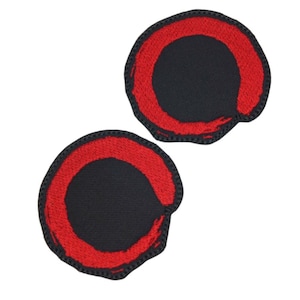 May include: Two red embroidered patches in the shape of a circle with a black center. The circle is a stylized brushstroke.