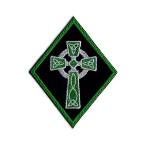 May include: Diamond-shaped embroidered patch with a Celtic cross design. The patch has a black background and a green border. The cross is white with green detailing, displaying detailed knotwork.