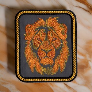 May include: A gray embroidered patch with a gold border featuring a lion's head with orange and yellow fur.