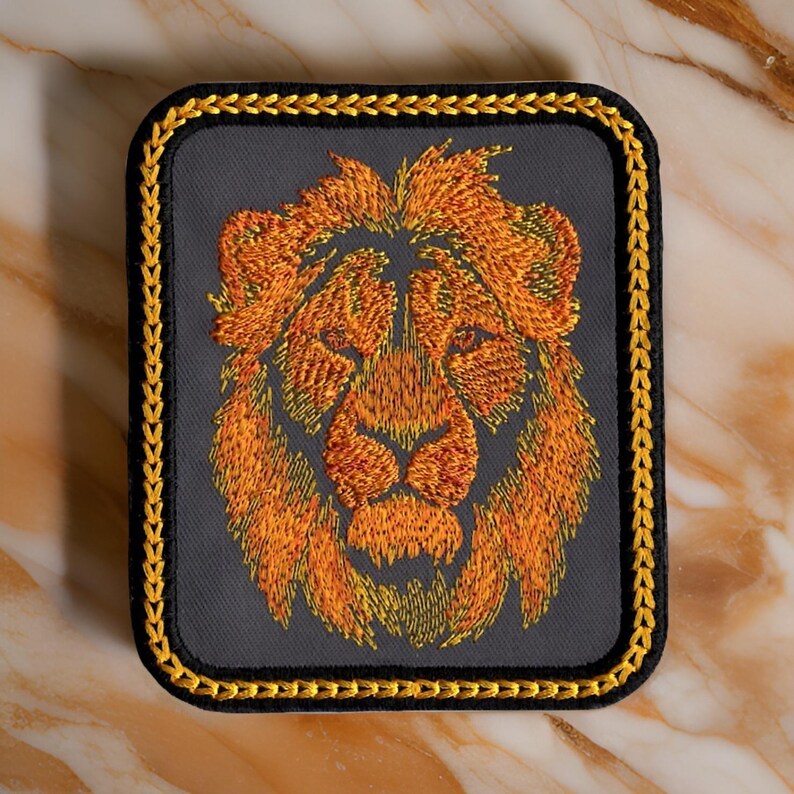 May include: A gray embroidered patch with a gold border featuring a lion's head with orange and yellow fur.