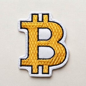 May include: A Bitcoin logo patch featuring a gold-coloured embroidered symbol with a textured diamond pattern. The design is outlined in black thread and bordered by a white fabric edge, creating a distinct shape of the cryptocurrency icon.
