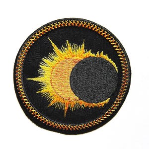 May include: Embroidered patch featuring a celestial design. The patch has a black background with a yellow and orange sun partially obscured by a black circle, resembling a solar eclipse. The border is stitched with orange thread.