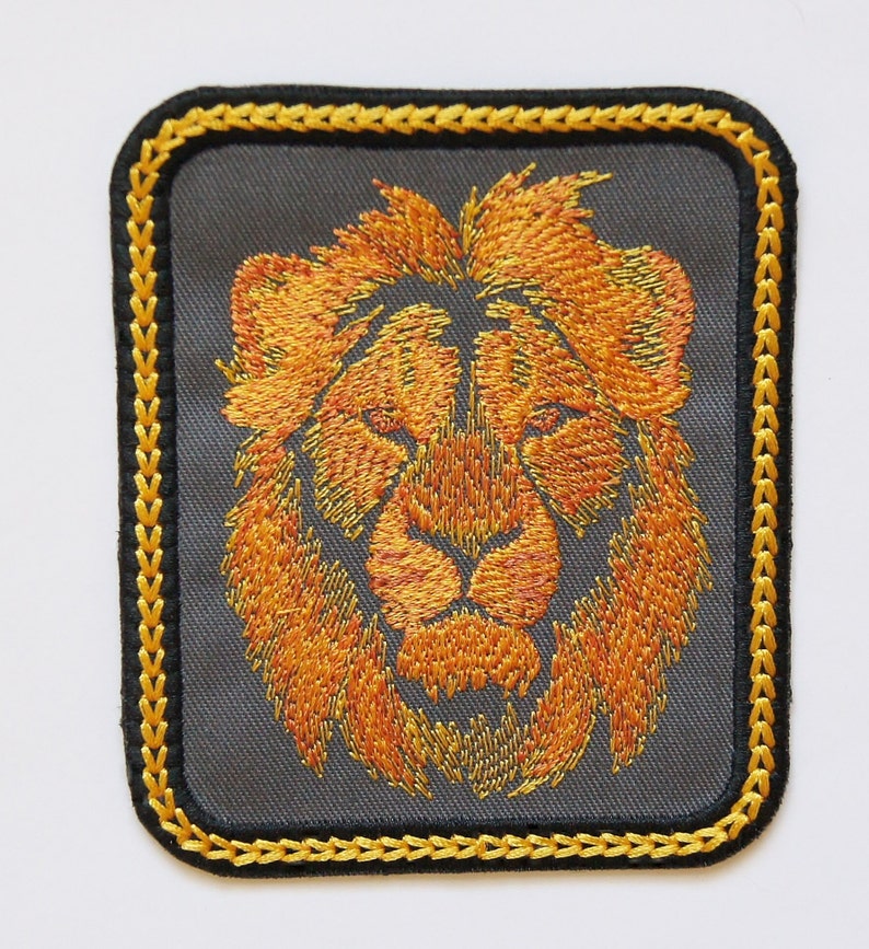 May include: Embroidered lion head patch with a gold outline on a gray background. The lion's mane is a vibrant orange color.
